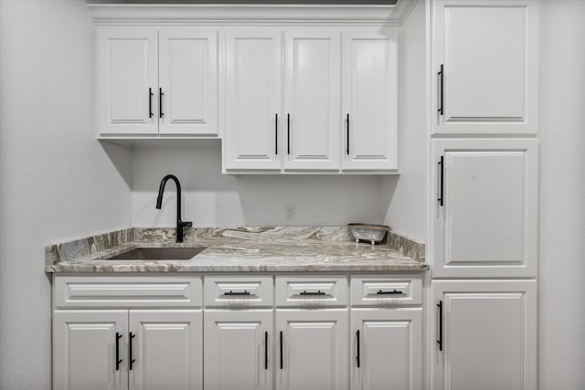 bar featuring white cabinets, light stone countertops, and sink