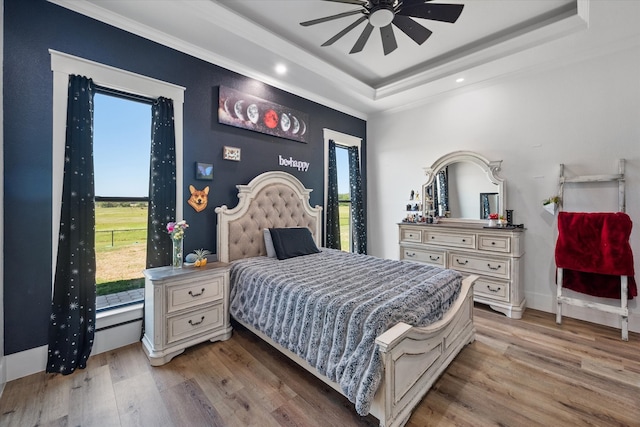 bedroom featuring a tray ceiling, ceiling fan, hardwood / wood-style flooring, and multiple windows