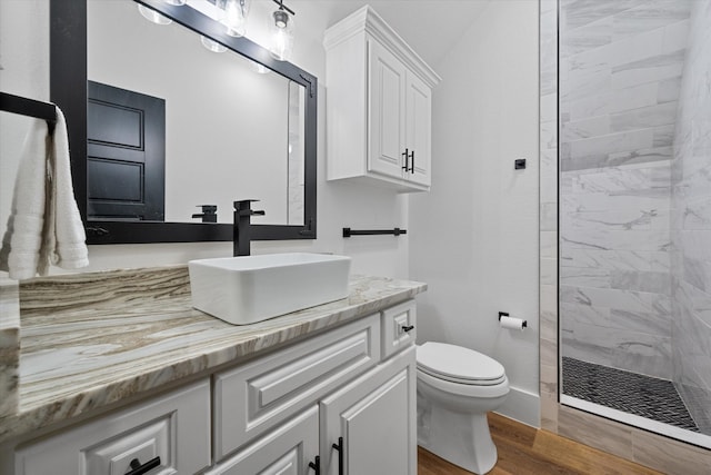 bathroom featuring a tile shower, hardwood / wood-style floors, vanity, and toilet