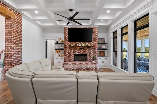 living room with light wood-type flooring, beamed ceiling, coffered ceiling, a fireplace, and ceiling fan