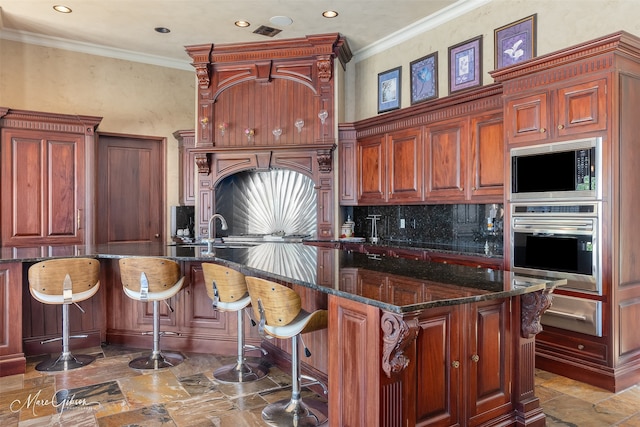 kitchen with decorative backsplash, a kitchen island with sink, stainless steel appliances, dark stone countertops, and crown molding