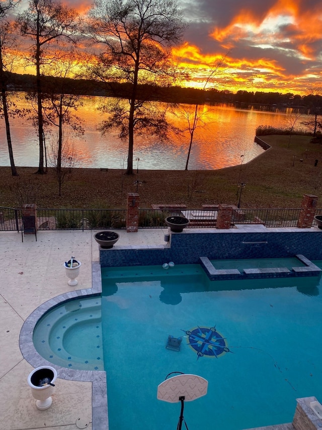 pool at dusk featuring a patio area, an in ground hot tub, and a water view