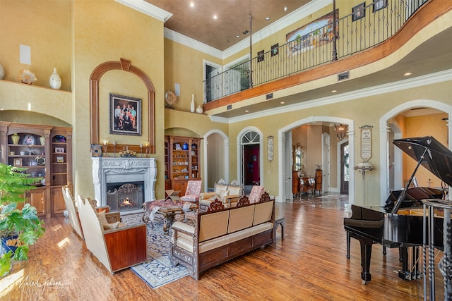 living room with a towering ceiling, a premium fireplace, hardwood / wood-style flooring, and ornamental molding