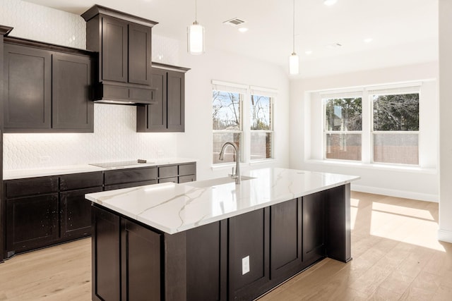 kitchen featuring an island with sink, sink, black electric cooktop, and decorative light fixtures