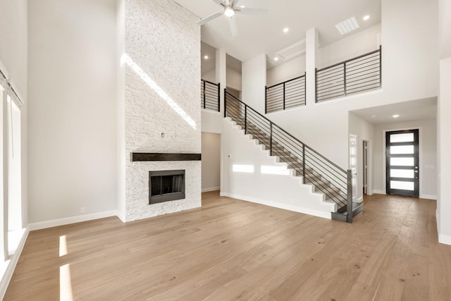 unfurnished living room with ceiling fan, a fireplace, light hardwood / wood-style floors, and a high ceiling