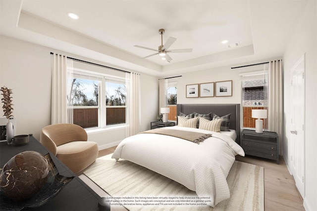 bedroom with a raised ceiling, ceiling fan, and light wood-type flooring