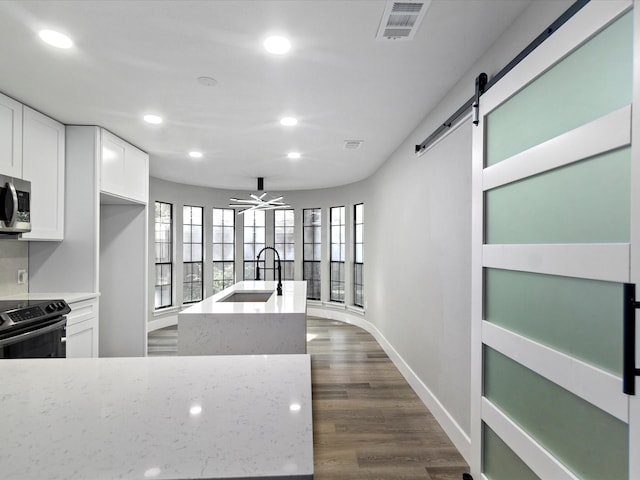 kitchen with dark wood-type flooring, sink, white cabinets, a barn door, and stainless steel appliances