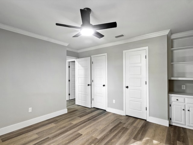 unfurnished bedroom with ceiling fan, ornamental molding, two closets, and dark wood-type flooring