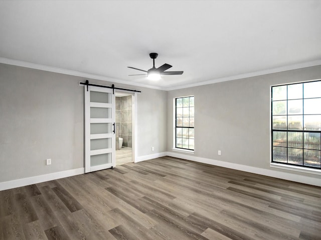 unfurnished bedroom featuring wood-type flooring, a barn door, ensuite bath, ornamental molding, and ceiling fan