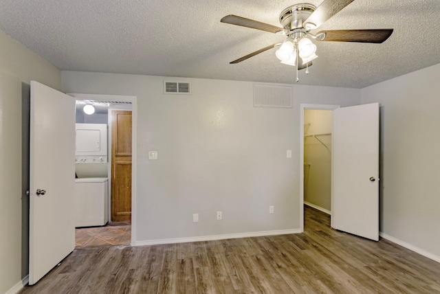 unfurnished bedroom featuring a textured ceiling, light hardwood / wood-style floors, a walk in closet, ceiling fan, and stacked washer and clothes dryer