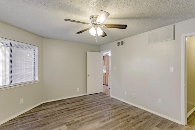 spare room featuring light wood-type flooring, a textured ceiling, and ceiling fan