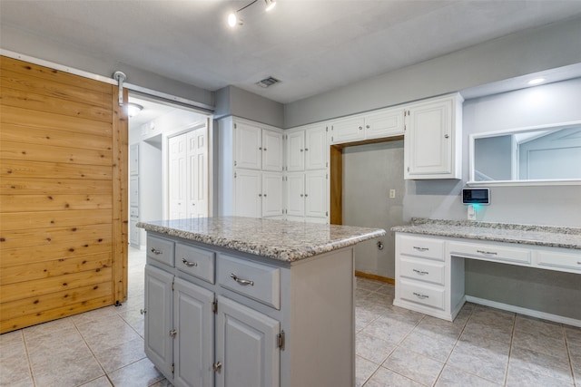 kitchen featuring white cabinetry, light stone counters, a barn door, a kitchen island, and light tile patterned floors