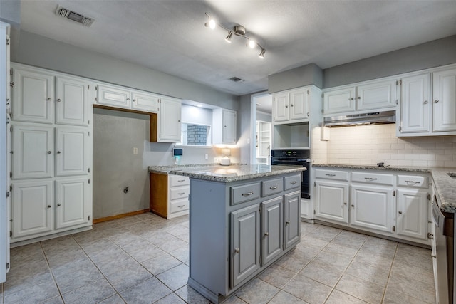 kitchen with white cabinets, black oven, light tile patterned floors, and a center island