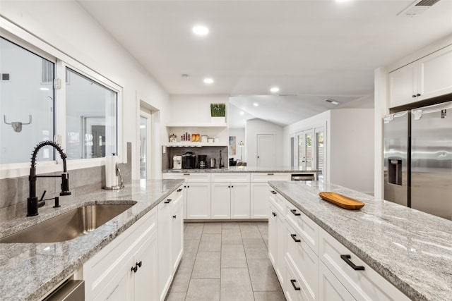 kitchen with lofted ceiling, white cabinetry, sink, and light stone counters