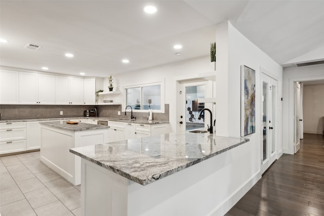 kitchen with light wood-type flooring, sink, a center island, light stone countertops, and decorative backsplash