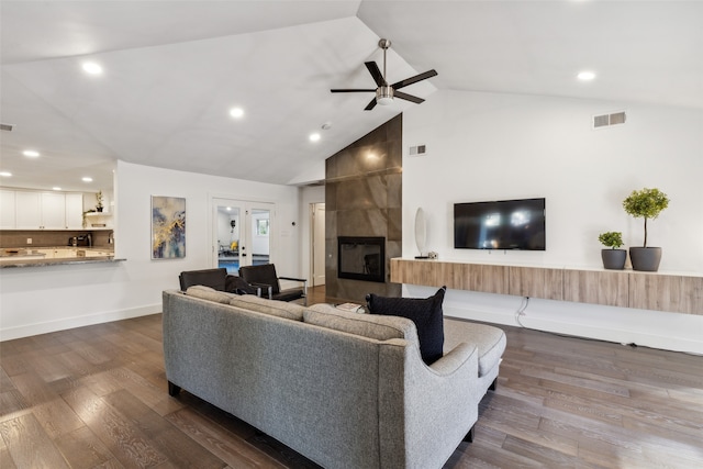 living room with high vaulted ceiling, ceiling fan, a tile fireplace, and dark wood-type flooring