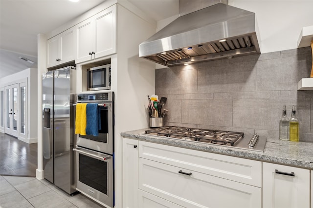 kitchen with appliances with stainless steel finishes, white cabinetry, backsplash, light tile patterned floors, and ventilation hood