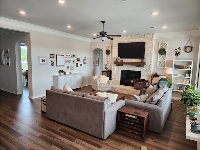 living room with ceiling fan, a stone fireplace, dark hardwood / wood-style floors, and crown molding