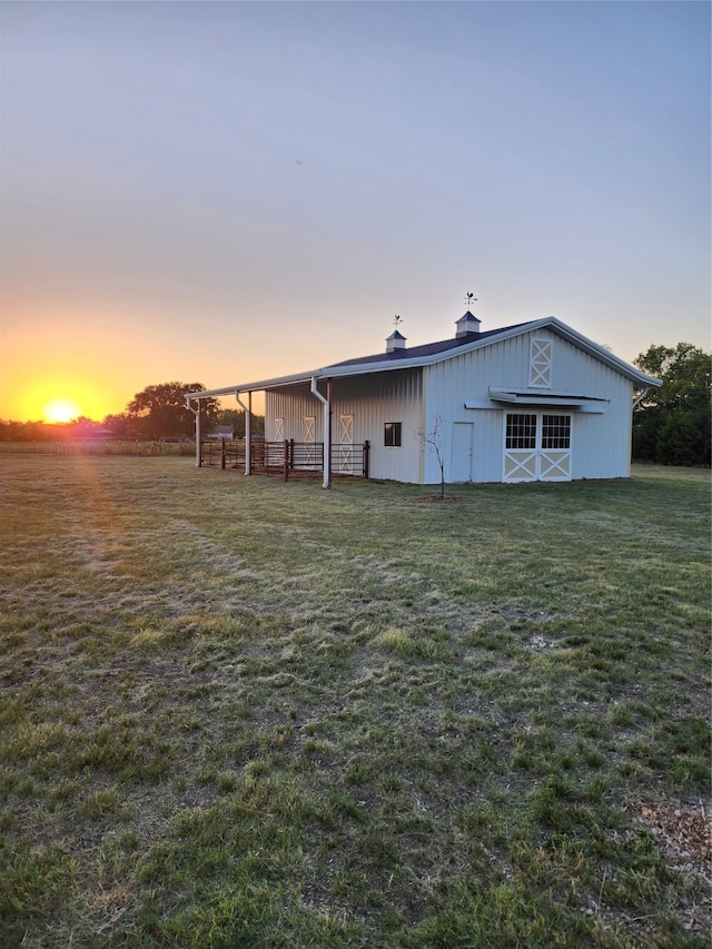 back house at dusk featuring a lawn and an outdoor structure