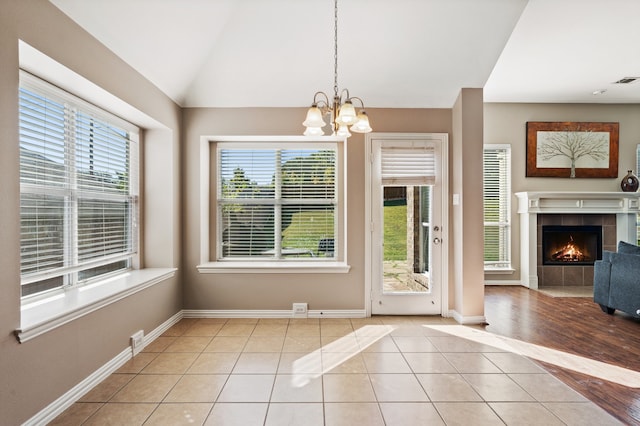 unfurnished dining area with an inviting chandelier, light tile patterned flooring, vaulted ceiling, and a healthy amount of sunlight