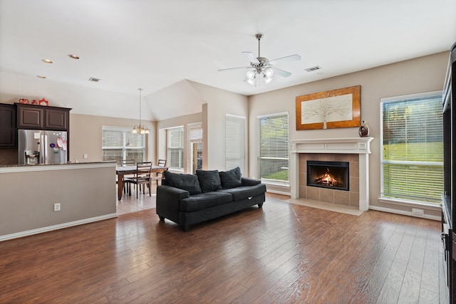 living room featuring ceiling fan with notable chandelier, a tiled fireplace, and dark wood-type flooring