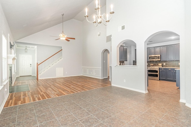 unfurnished living room featuring ceiling fan with notable chandelier, light hardwood / wood-style flooring, and high vaulted ceiling