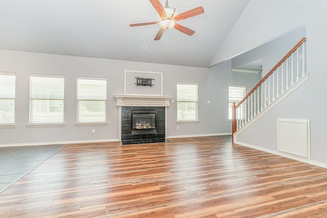 unfurnished living room featuring ceiling fan, light wood-type flooring, high vaulted ceiling, and a tiled fireplace