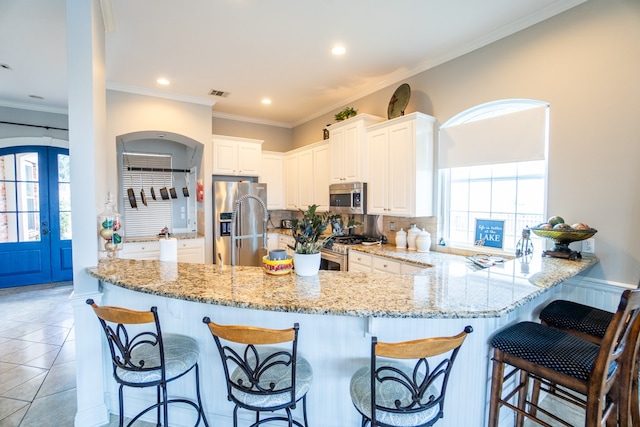 kitchen with ornamental molding, kitchen peninsula, backsplash, white cabinetry, and appliances with stainless steel finishes