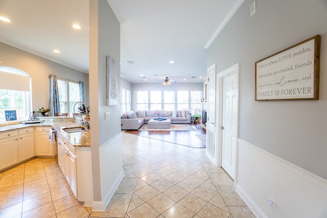 kitchen with light wood-type flooring, light stone counters, sink, crown molding, and ceiling fan