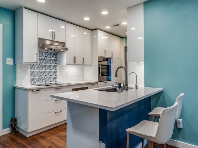 kitchen featuring dark wood-type flooring, sink, a breakfast bar area, white cabinets, and oven