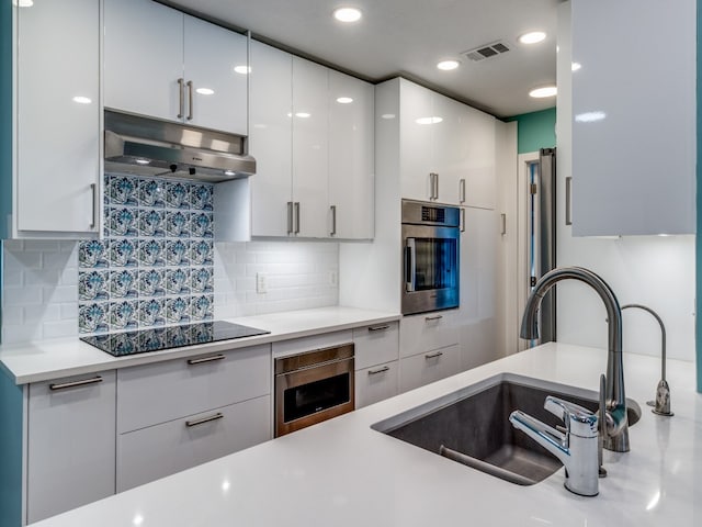 kitchen featuring black electric stovetop, oven, sink, and white cabinets