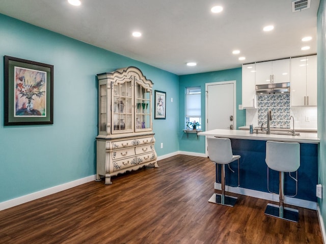 kitchen with a breakfast bar area, dark hardwood / wood-style flooring, decorative backsplash, and white cabinetry