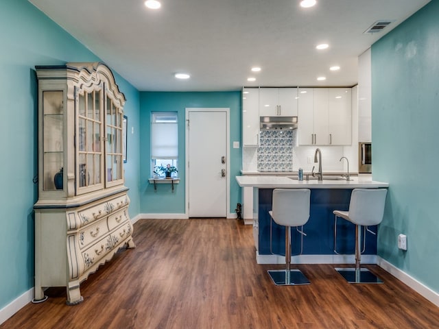 kitchen featuring kitchen peninsula, sink, white cabinetry, a breakfast bar, and dark hardwood / wood-style flooring