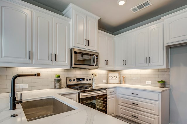 kitchen featuring tasteful backsplash, sink, white cabinetry, appliances with stainless steel finishes, and light stone counters