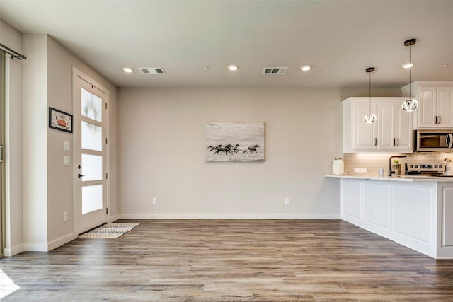 kitchen with white cabinetry, appliances with stainless steel finishes, decorative backsplash, pendant lighting, and light hardwood / wood-style flooring