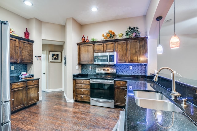 kitchen with dark wood-type flooring, tasteful backsplash, pendant lighting, stainless steel appliances, and sink