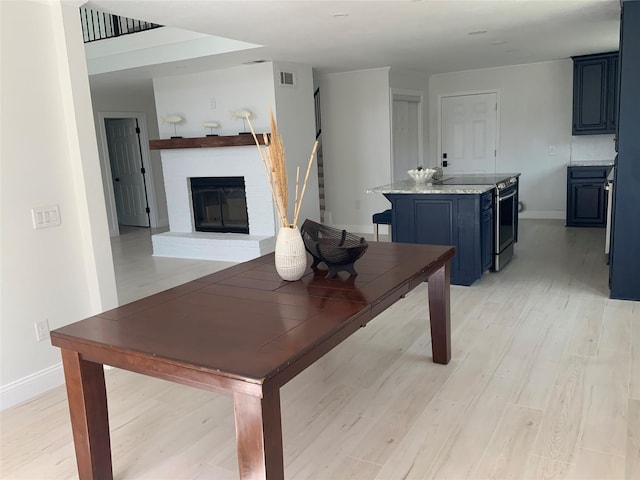 dining area with visible vents, baseboards, light wood finished floors, a fireplace, and stairs