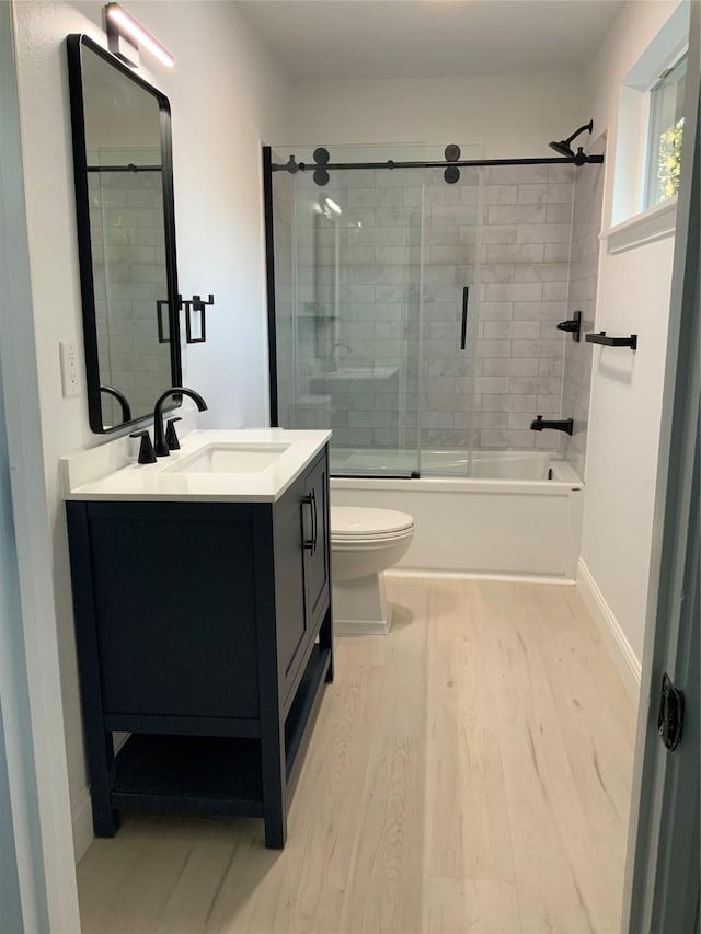 bathroom featuring vanity, wood finished floors, baseboards, enclosed tub / shower combo, and toilet