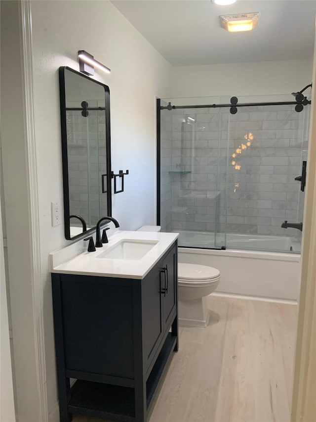 bathroom with enclosed tub / shower combo, toilet, wood finished floors, and vanity