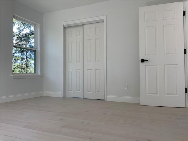 unfurnished bedroom featuring baseboards, light wood-type flooring, and a closet