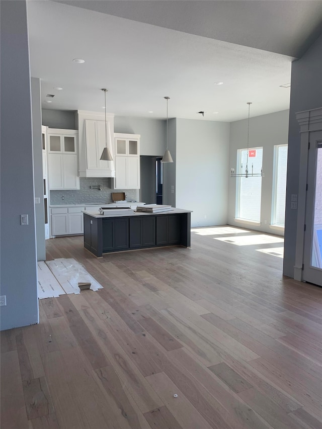 kitchen featuring white cabinets, pendant lighting, tasteful backsplash, a kitchen island with sink, and light hardwood / wood-style flooring