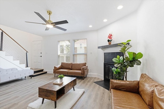 living room featuring a tile fireplace, ceiling fan, and light hardwood / wood-style flooring