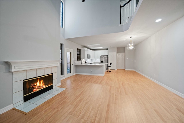 unfurnished living room with light wood-type flooring, a towering ceiling, and a tile fireplace