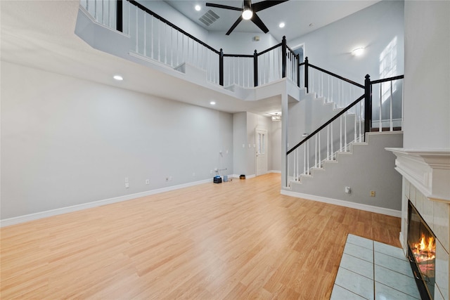 unfurnished living room with a tile fireplace, a towering ceiling, light hardwood / wood-style flooring, and ceiling fan