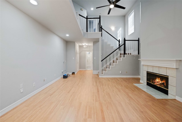 unfurnished living room featuring ceiling fan, light hardwood / wood-style flooring, a fireplace, and a high ceiling