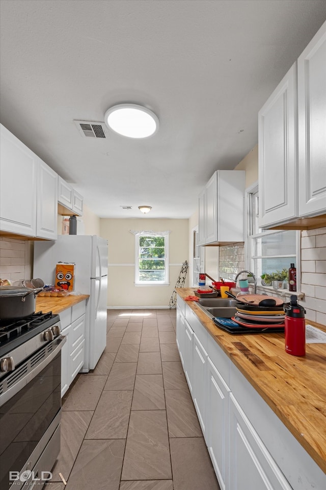 kitchen featuring stainless steel gas stove, white cabinetry, butcher block counters, and tasteful backsplash