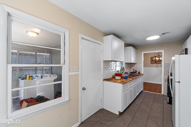 kitchen featuring white refrigerator, washer and dryer, wooden counters, and white cabinetry