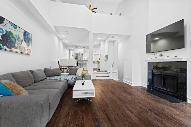 living room featuring a high ceiling, dark hardwood / wood-style flooring, ceiling fan, and a premium fireplace