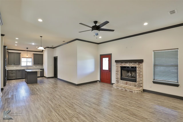 unfurnished living room featuring a brick fireplace, ceiling fan, hardwood / wood-style flooring, ornamental molding, and sink