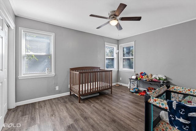 bedroom featuring ceiling fan, hardwood / wood-style flooring, a crib, and multiple windows